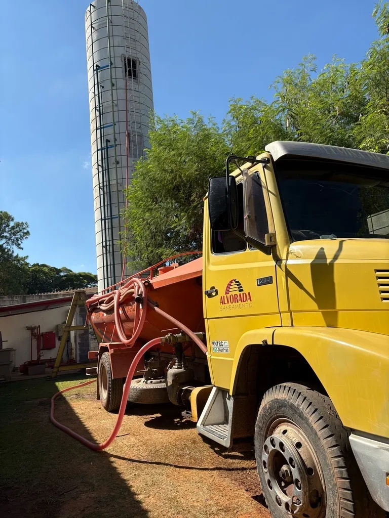 Caminhão pipa amarelo junto a torre de água